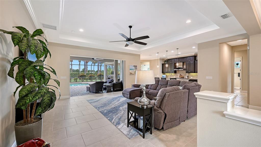 A living room with a sectional sofa, tray ceiling, and sliding doors opening to a pool — 8215 LARKSPUR CIRCLE, SARASOTA, FL