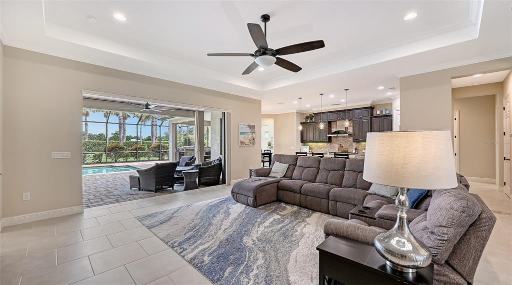 A spacious living room with a large sectional sofa opens to a covered patio and pool — 8215 LARKSPUR CIRCLE, SARASOTA, FL