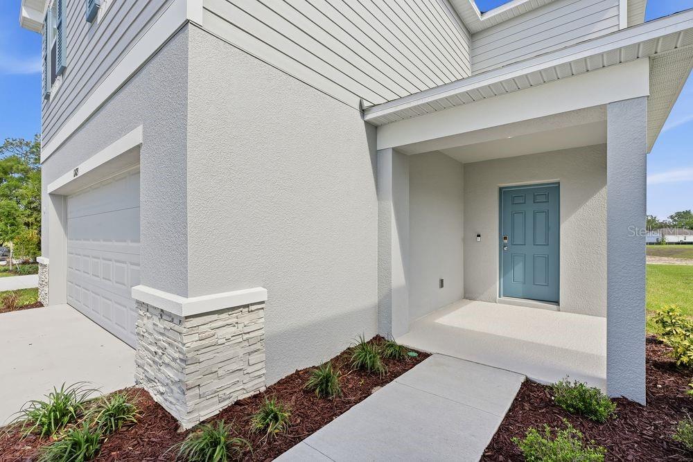 A light gray house exterior features a blue front door, stone accents, and a concrete walkway — 12423 WHISK COURT, HUDSON, FL