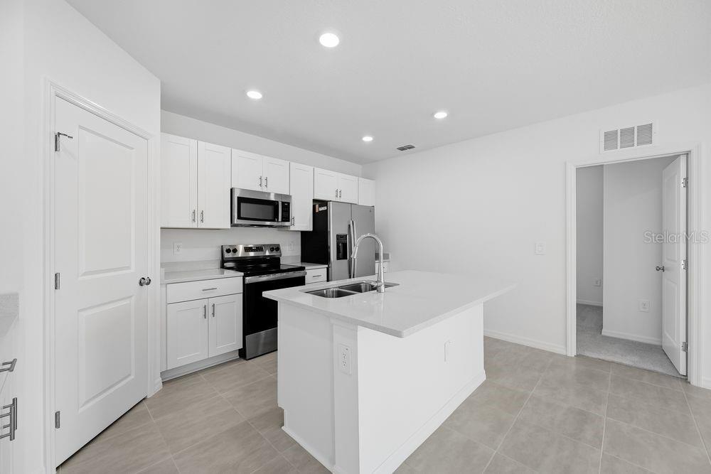 A modern kitchen features white cabinetry, stainless steel appliances, and a central island with seating — 12423 WHISK COURT, HUDSON, FL