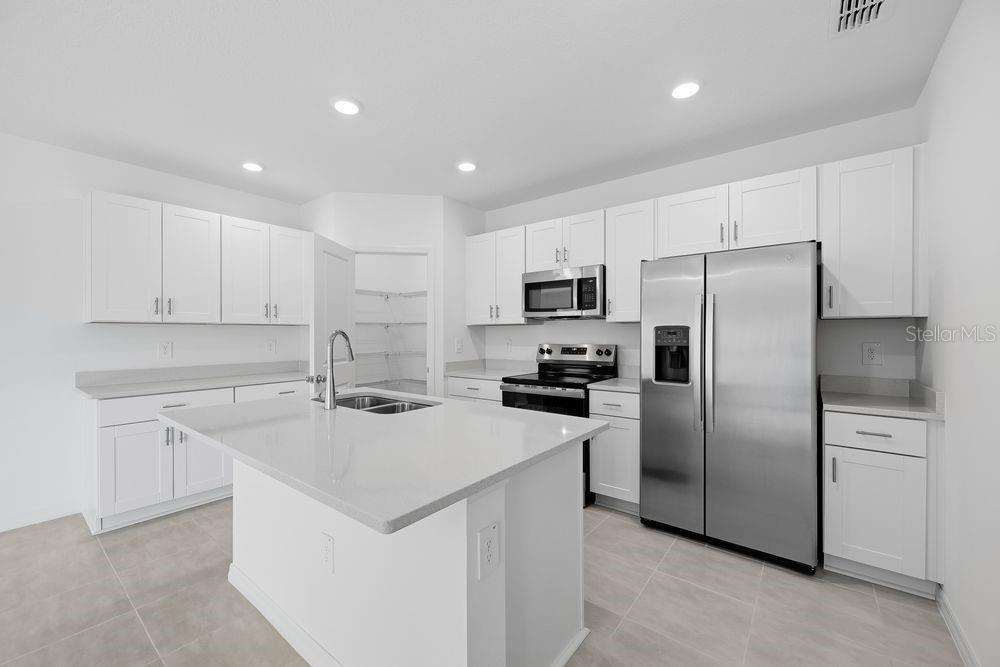 A modern kitchen features white cabinets, stainless steel appliances, a center island, and tile flooring — 12423 WHISK COURT, HUDSON, FL