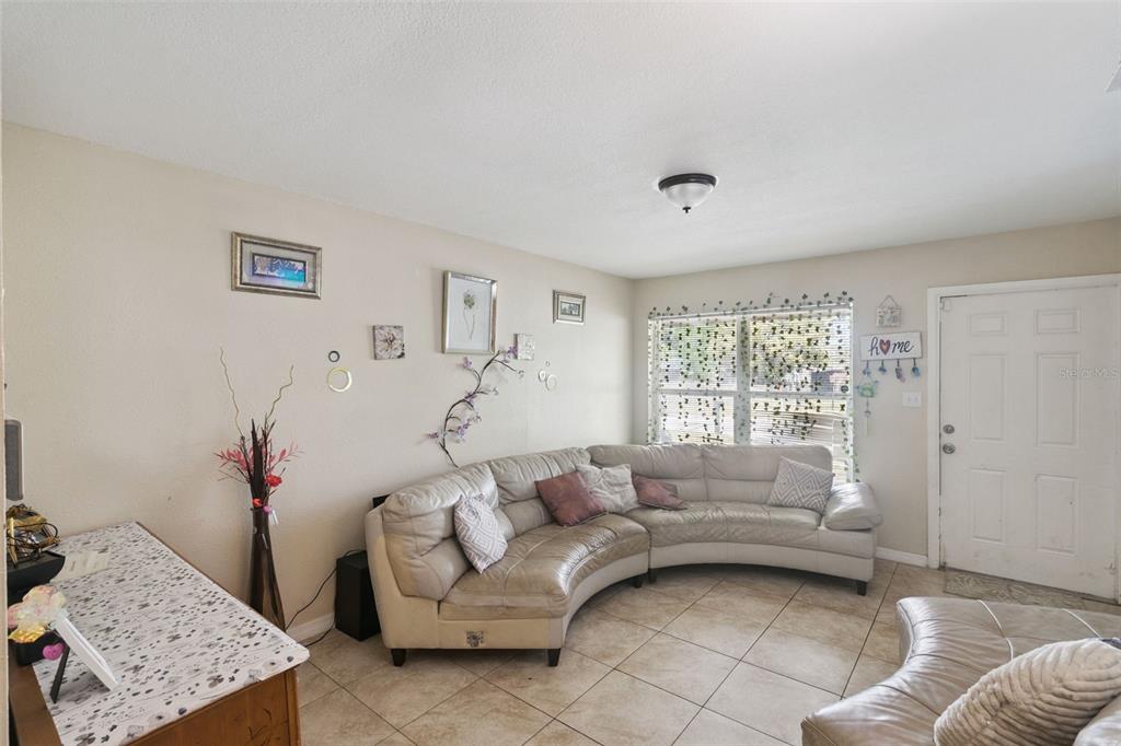 A living room features a curved sectional sofa, tile flooring, and a window with hanging greenery — 4366 KIRKLAND BOULEVARD, ORLANDO, FL