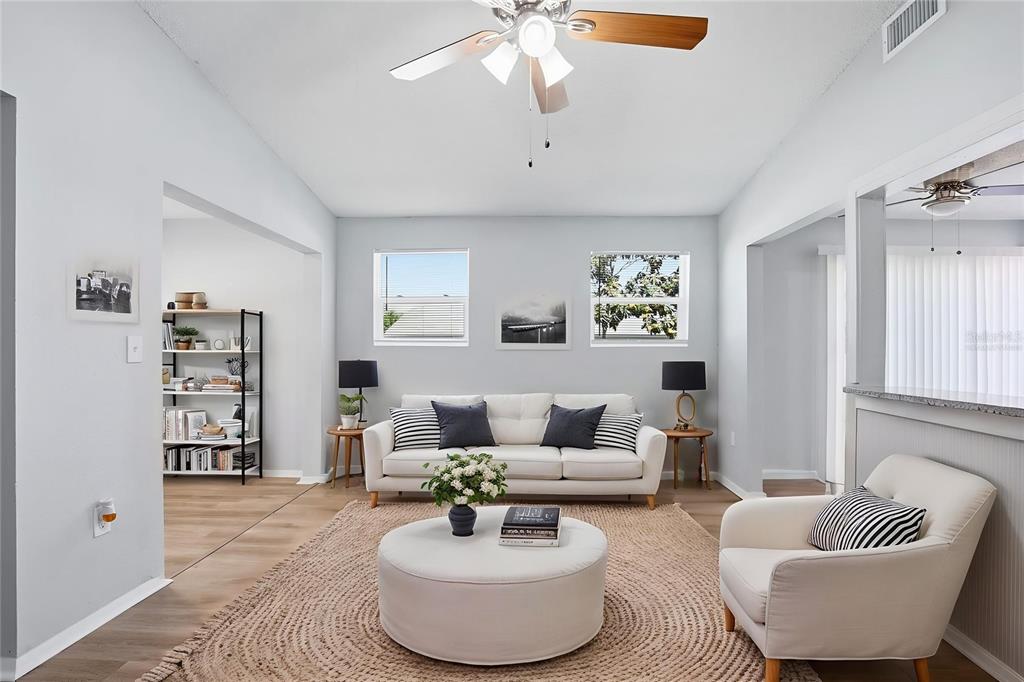 A bright living room features a white sofa, round ottoman, and light wood-look flooring — 728 E SPRUCE STREET, TARPON SPRINGS, FL