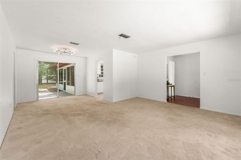 A spacious living room with beige carpet, white walls, and a sliding glass door — 2413 NW 63RD TERRACE, GAINESVILLE, FL