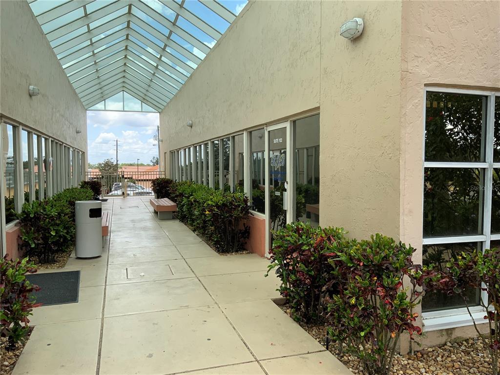 An outdoor walkway with a glass roof leads past office suites and landscaped bushes — 3205 MEDICAL WAY UNIT 104, SEBRING, FL