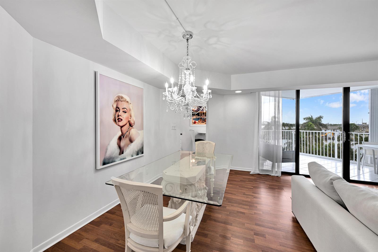 A dining area features a glass table, white chairs, a crystal chandelier, and Marilyn Monroe art — 2860 S Ocean Boulevard # 511, Palm Beach FL 33480, PALM BEACH, FL