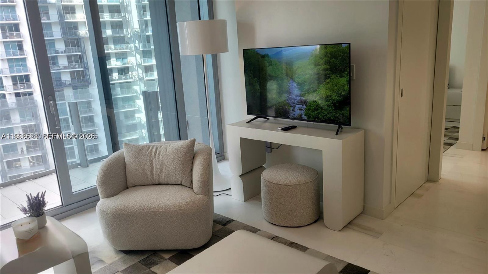 A modern living room features a white console table, a textured armchair, and floor-to-ceiling windows — 300 Biscayne Blvd Way # 2908, Miami FL 33131, MIAMI, FL