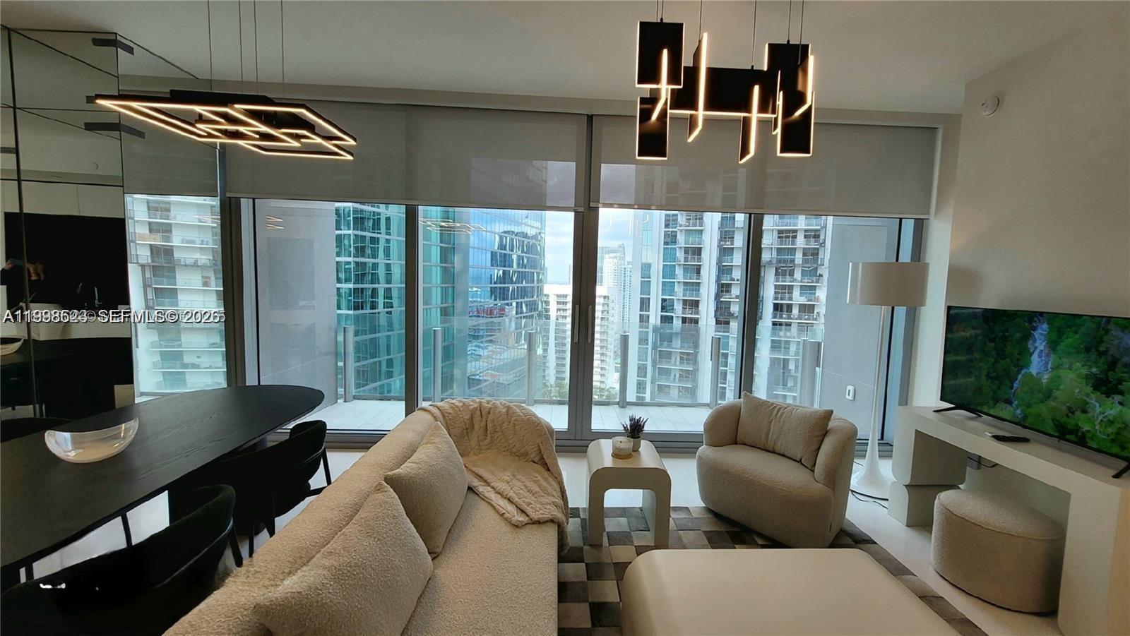 A modern living room features floor-to-ceiling windows, contemporary light fixtures, and neutral-toned furniture — 300 Biscayne Blvd Way # 2908, Miami FL 33131, MIAMI, FL