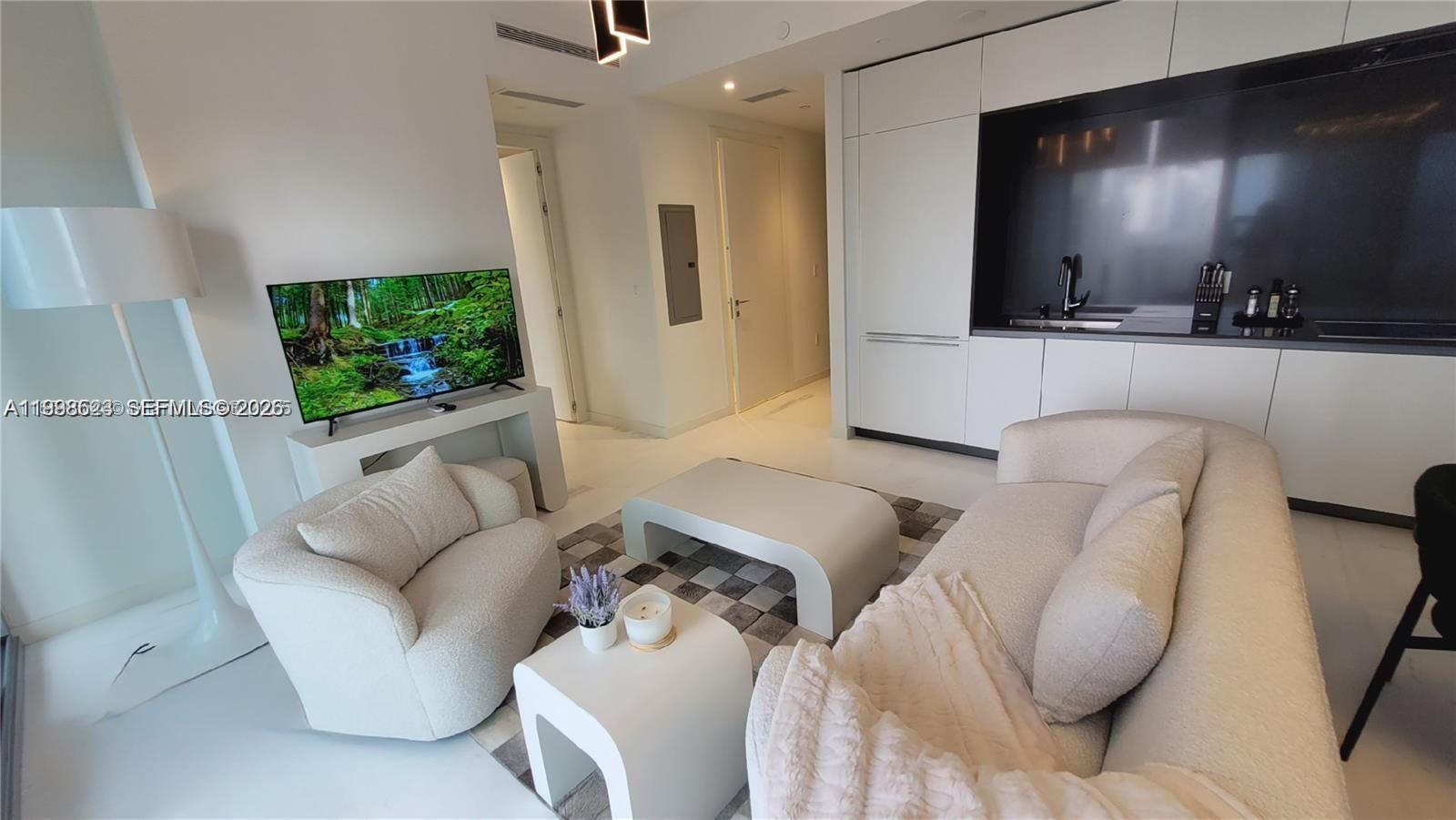 A modern living room features white furniture, a television, and an integrated kitchen area — 300 Biscayne Blvd Way # 2908, Miami FL 33131, MIAMI, FL