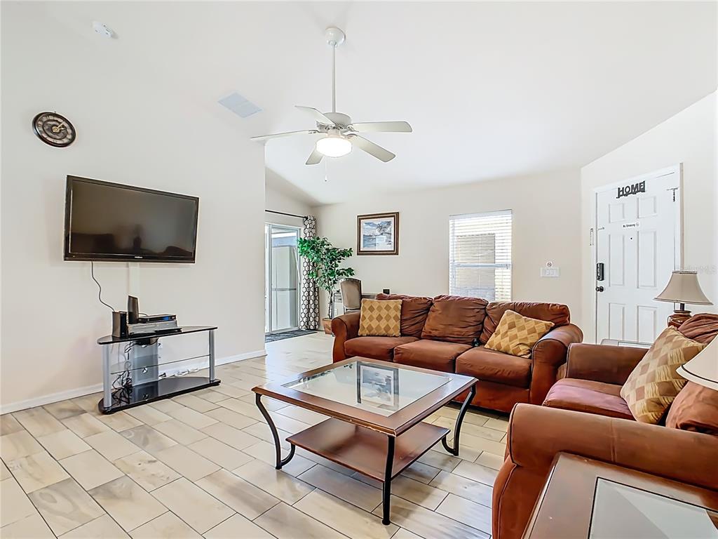A living room features tile flooring, a brown sofa set, a glass coffee table, and a ceiling fan — 1958 ROYAL RIDGE DRIVE, DAVENPORT, FL