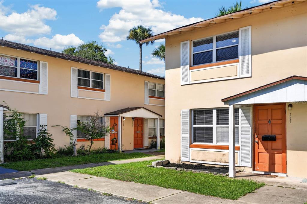 A two-story apartment building with tan stucco walls, orange doors, and white window shutters — 1600 S PALMETTO AVENUE UNIT 111, SOUTH DAYTONA, FL