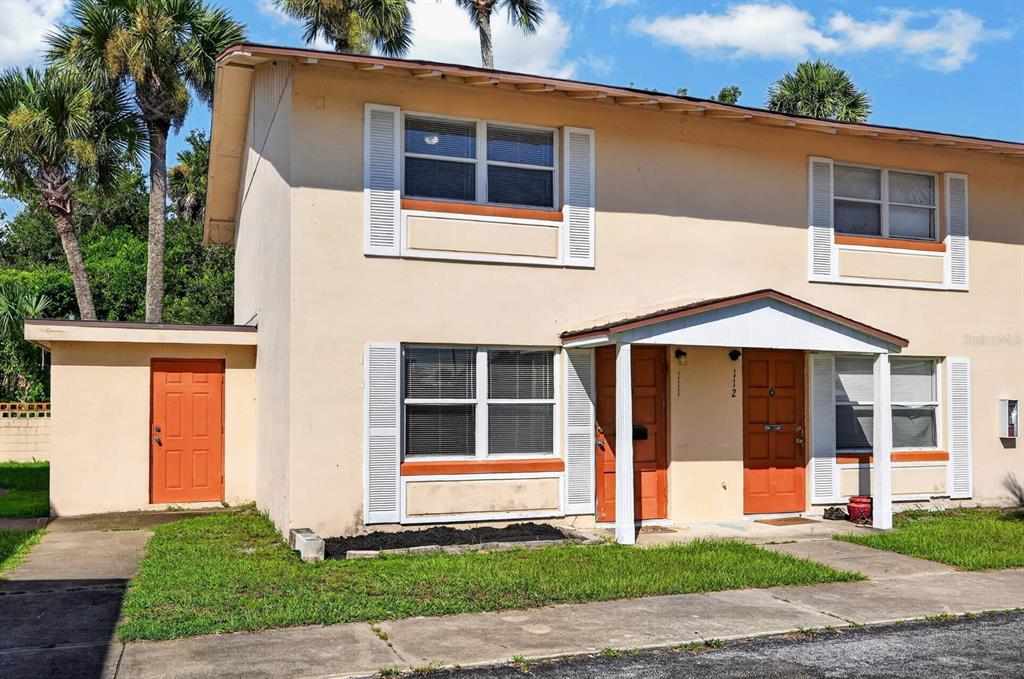 A two-story beige apartment building with orange doors and white shutters under a blue sky — 1600 S PALMETTO AVENUE UNIT 111, SOUTH DAYTONA, FL