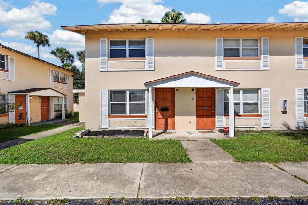 A two-story apartment building exterior features tan stucco walls, orange doors, and white window shutters — 1600 S PALMETTO AVENUE UNIT 111, SOUTH DAYTONA, FL