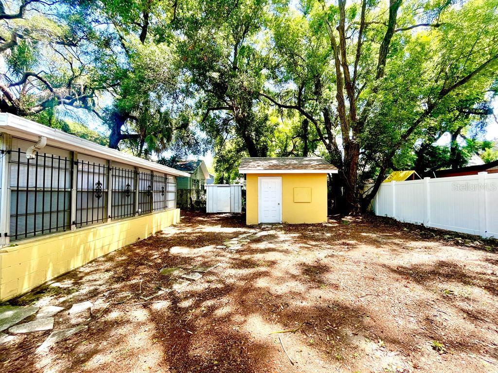 A yellow shed stands in a backyard with a white fence and large shade trees — 1003 E 22ND AVENUE, TAMPA, FL