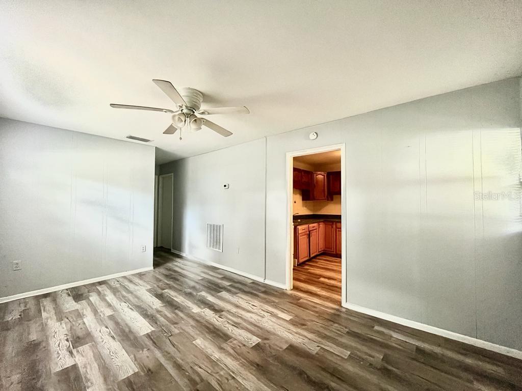 A living room with gray walls, wood-look flooring, a ceiling fan, and a kitchen doorway — 1003 E 22ND AVENUE, TAMPA, FL