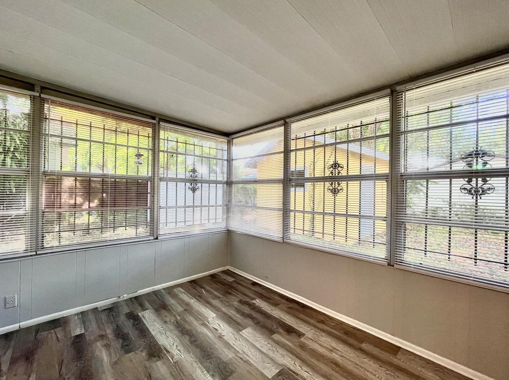 A sunroom with wood-look flooring, gray paneled walls, and windows covered by horizontal blinds — 1003 E 22ND AVENUE, TAMPA, FL
