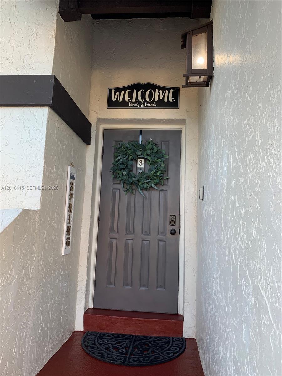A gray front door with a wreath and a welcome sign sits in a recessed entryway — 11325 SW 133rd Ct # 3, Miami FL 33186, MIAMI, FL