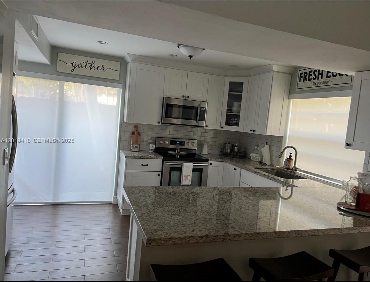 A kitchen features white cabinets, granite countertops, stainless steel appliances, and dark wood flooring — 11325 SW 133rd Ct # 3, Miami FL 33186, MIAMI, FL