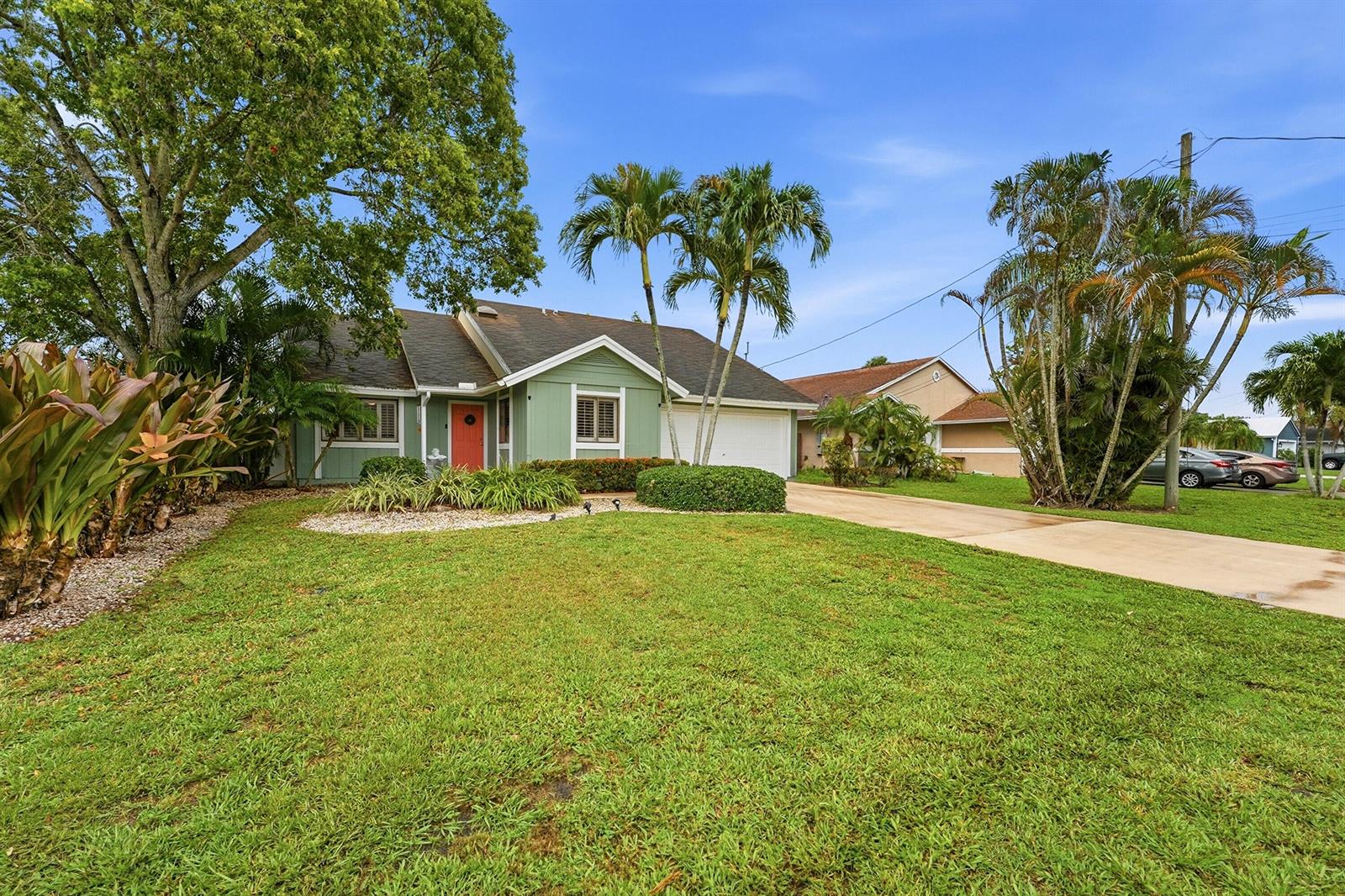 A single-story green house with a white garage and a front lawn with palm trees — 6273 Barbara Street, Jupiter FL 33458, JUPITER, FL