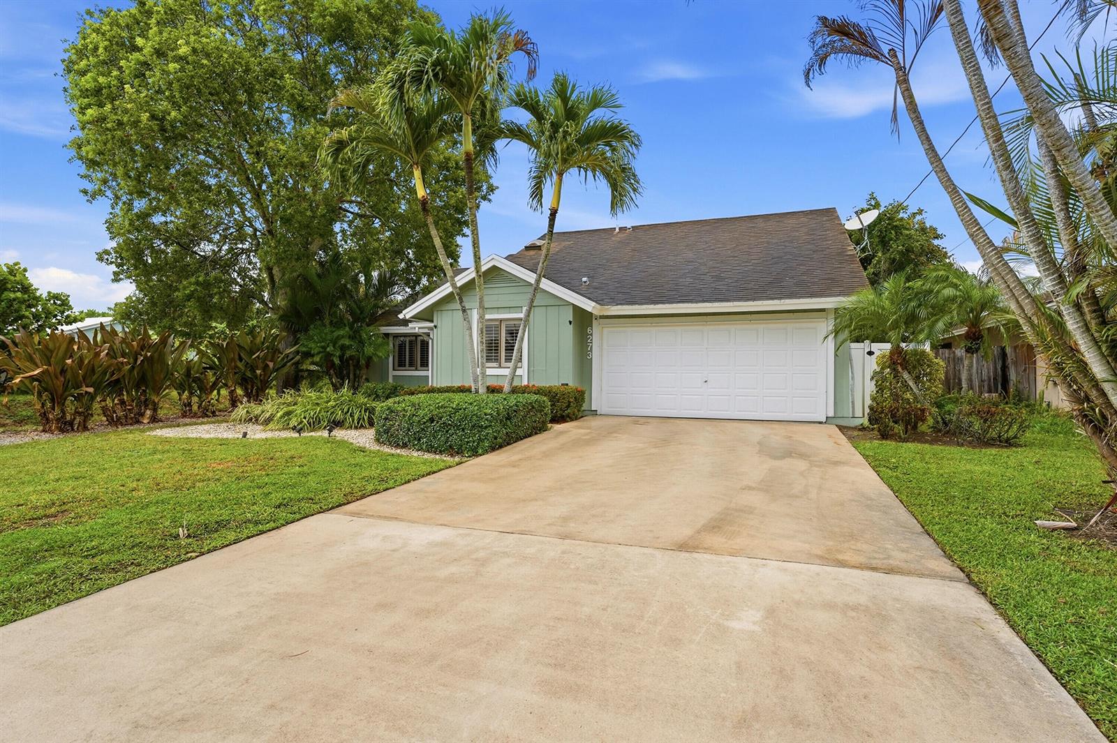 A single-story house with light green siding, a white garage door, and palm trees — 6273 Barbara Street, Jupiter FL 33458, JUPITER, FL