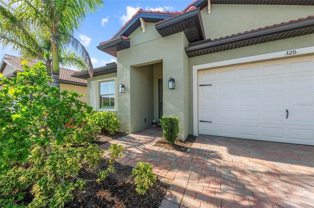 A light green house exterior features a brick paver walkway and a white garage door — 325 VILLORESI BOULEVARD, NOKOMIS, FL