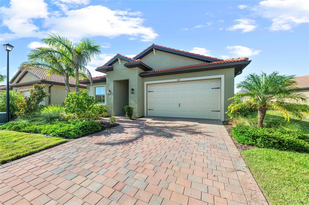 A single-story house with a beige stucco exterior, a two-car garage, and a paver driveway — 325 VILLORESI BOULEVARD, NOKOMIS, FL
