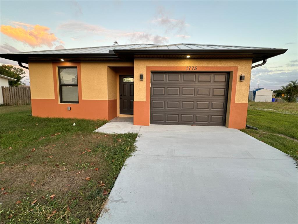 A single-story house with a two-tone stucco exterior, a metal roof, and a concrete driveway — 1775 GLENWAY COURT, FORT MYERS, FL