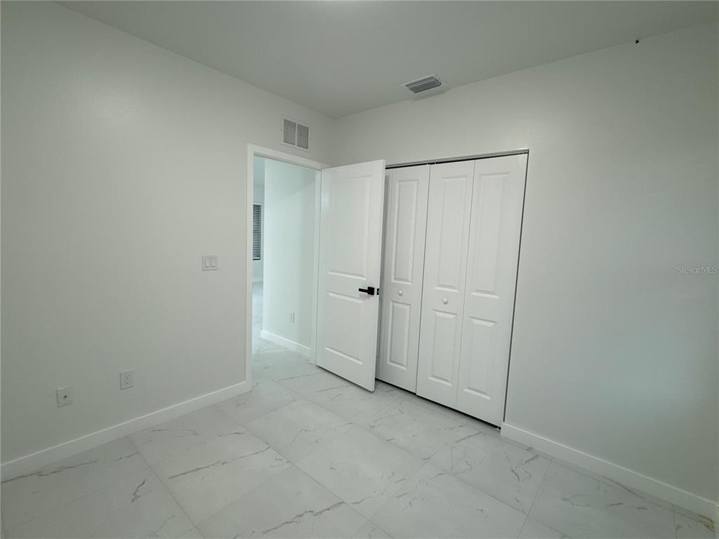 A bedroom features white walls, light-colored tile flooring, and a white bi-fold closet door — 1775 GLENWAY COURT, FORT MYERS, FL