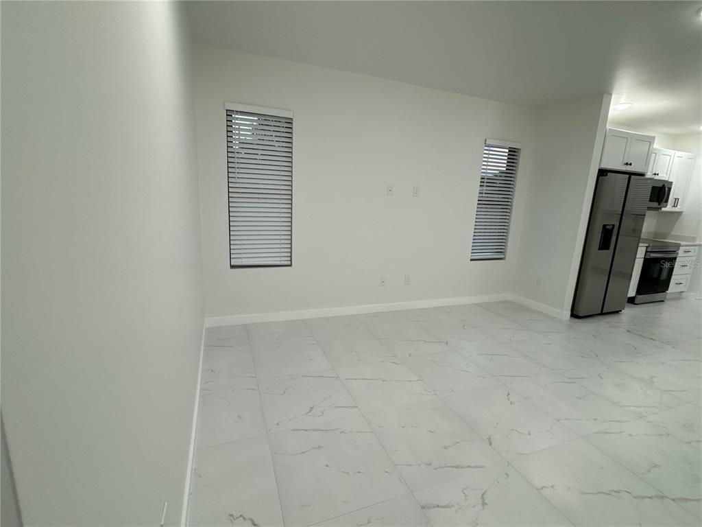 An open-concept living area features white walls, large marble-look floor tiles, and two windows — 1775 GLENWAY COURT, FORT MYERS, FL