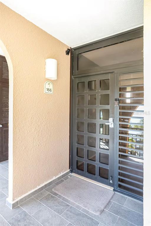 An exterior entryway features a gray grid-patterned door, a light fixture, and tiled flooring — 166 BEACH VILLAGE, HUMACAO, PR