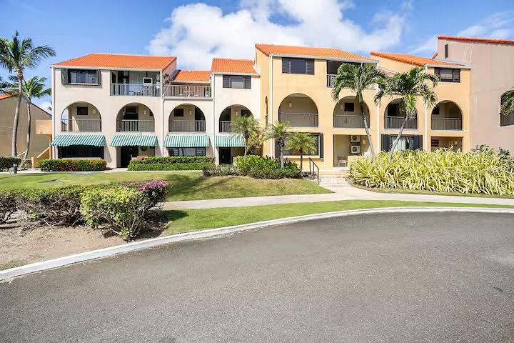 A multi-story apartment building with arched balconies, orange tile roofs, and palm trees — 166 BEACH VILLAGE, HUMACAO, PR
