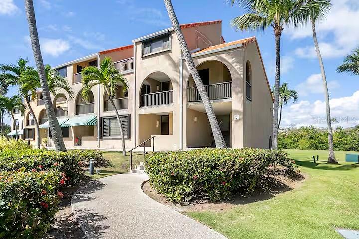 A multi-story tan stucco apartment building with arched balconies and palm trees — 166 BEACH VILLAGE, HUMACAO, PR