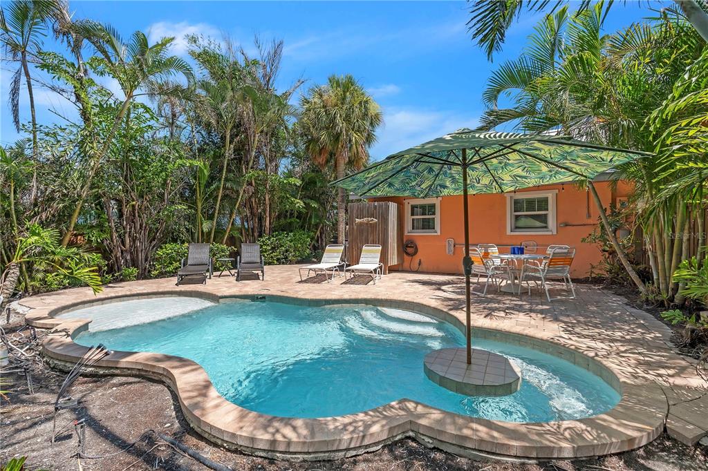 A backyard swimming pool with a patio, lounge chairs, dining set, and a large umbrella — 205 PEACOCK LANE UNIT A, HOLMES BEACH, FL