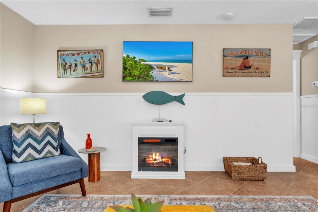 A living room features a blue armchair, a fireplace, a television, and beach-themed wall art — 205 PEACOCK LANE UNIT A, HOLMES BEACH, FL