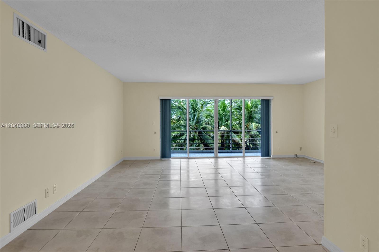 An empty living room features light-colored tile flooring, pale yellow walls, and a sliding glass door — 1000 NE 14th Ave # 503, Hallandale Beach FL 33009, HALLANDALE BEACH, FL