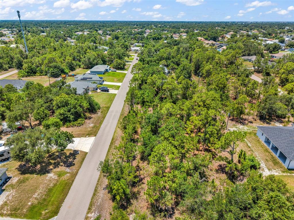 An aerial view shows a paved road running between a wooded lot and residential houses — 325 WYLER STREET, PORT CHARLOTTE, FL