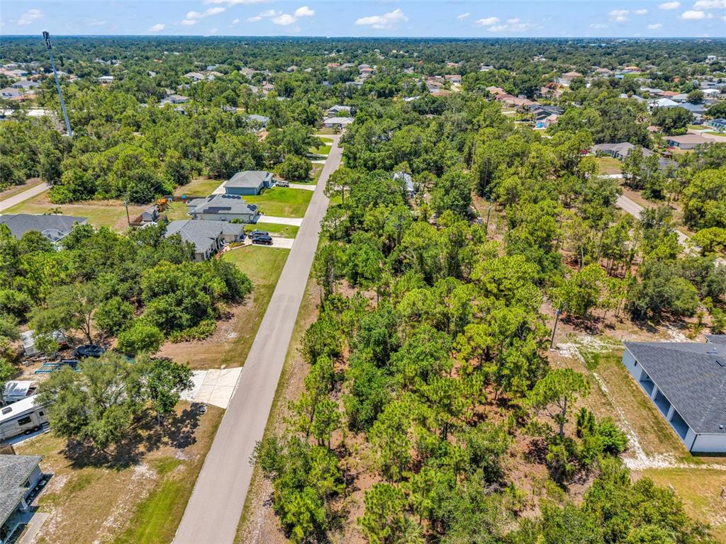 An aerial view shows a paved road running between a wooded lot and residential houses — 325 WYLER STREET, PORT CHARLOTTE, FL
