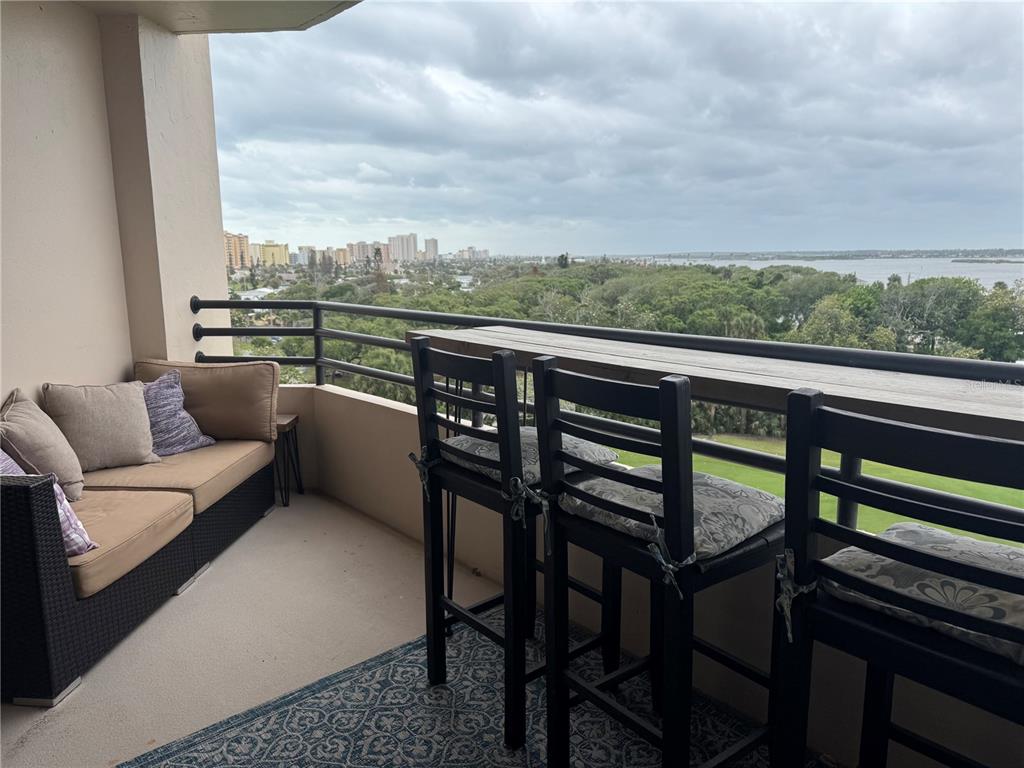 A balcony features a sofa, bar-style seating, and a view of a city and water — 1 OCEANS WEST BOULEVARD UNIT 6B1, DAYTONA BEACH, FL