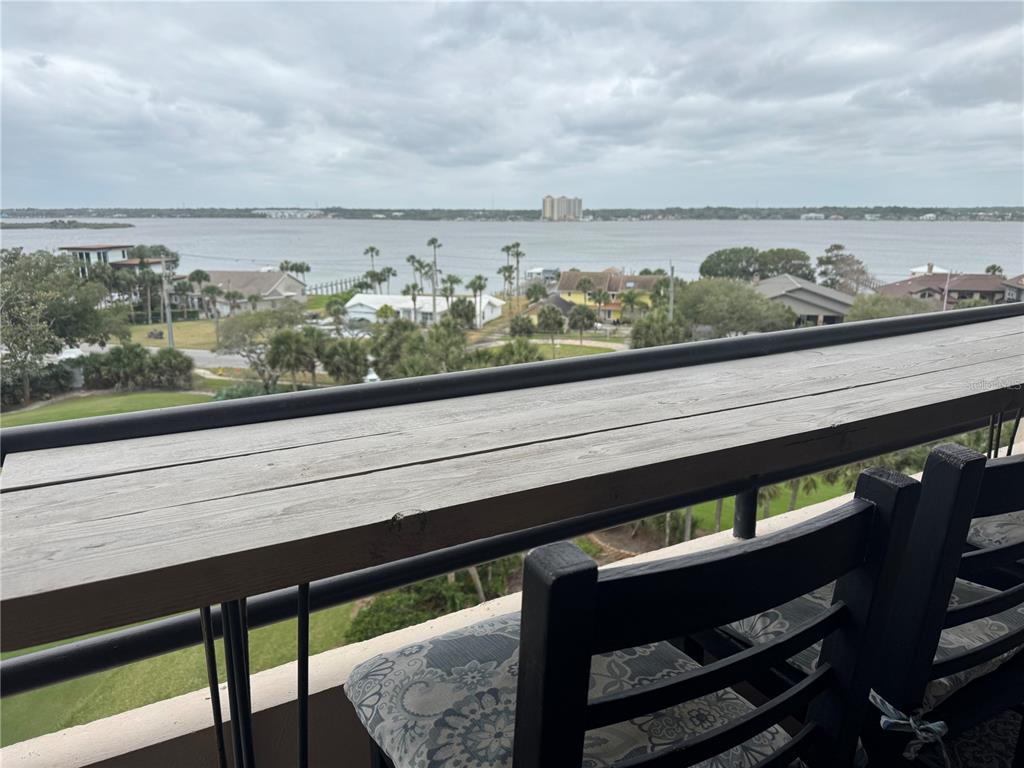 A balcony features a wooden bar table overlooking a body of water and coastal homes — 1 OCEANS WEST BOULEVARD UNIT 6B1, DAYTONA BEACH, FL