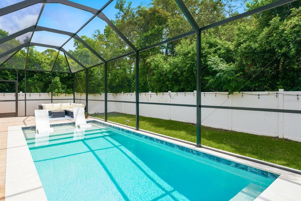 A rectangular swimming pool with lounge chairs sits inside a screened-in patio with a lawn — 11632 WEAVER HOLLOW ROAD, NEW PORT RICHEY, FL