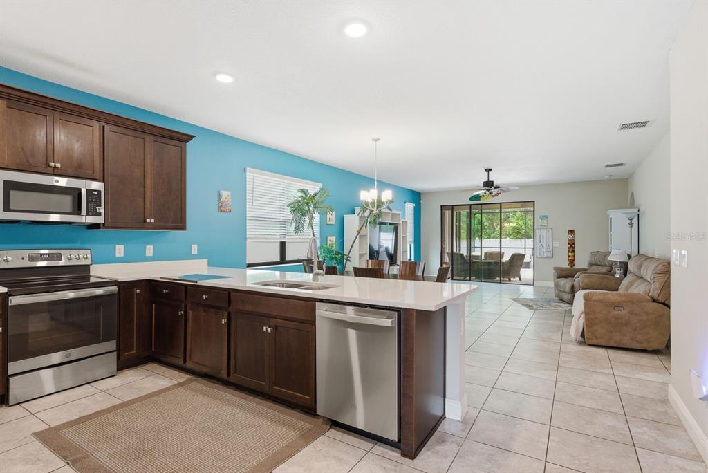 A kitchen with dark wood cabinets and stainless steel appliances opens into a living area — 11632 WEAVER HOLLOW ROAD, NEW PORT RICHEY, FL