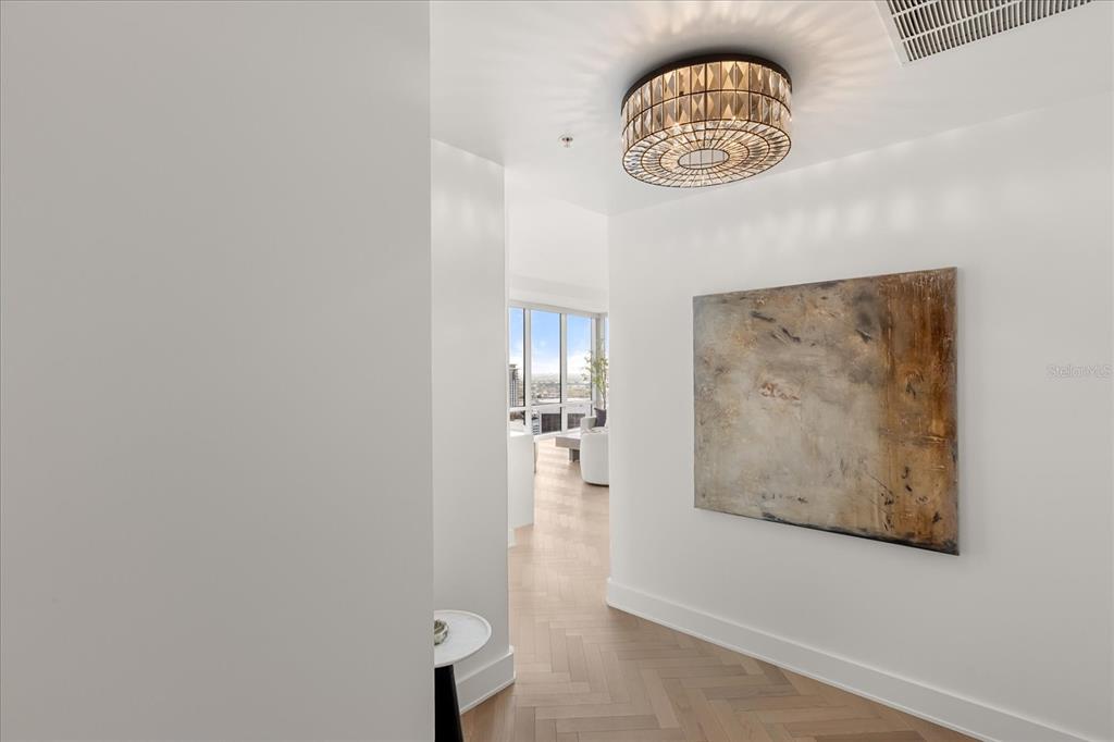 A hallway with light wood herringbone floors leads to a bright living area with windows — 150 E ROBINSON STREET UNIT 30C-2, ORLANDO, FL