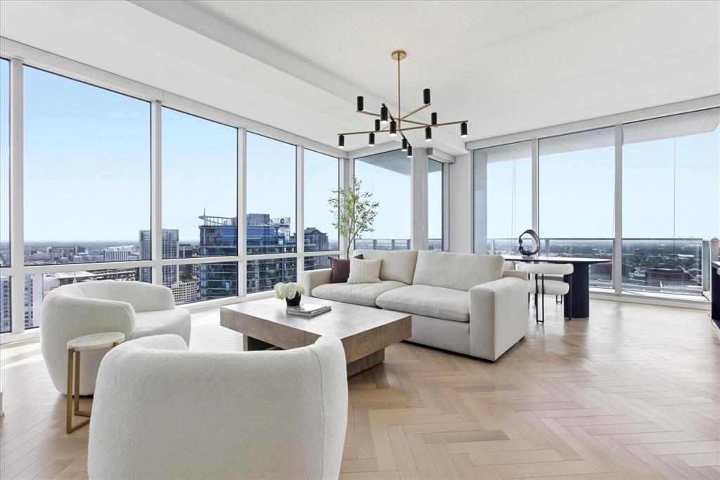 A modern living room features floor-to-ceiling windows, light wood herringbone floors, and a contemporary chandelier — 150 E ROBINSON STREET UNIT 30C-2, ORLANDO, FL