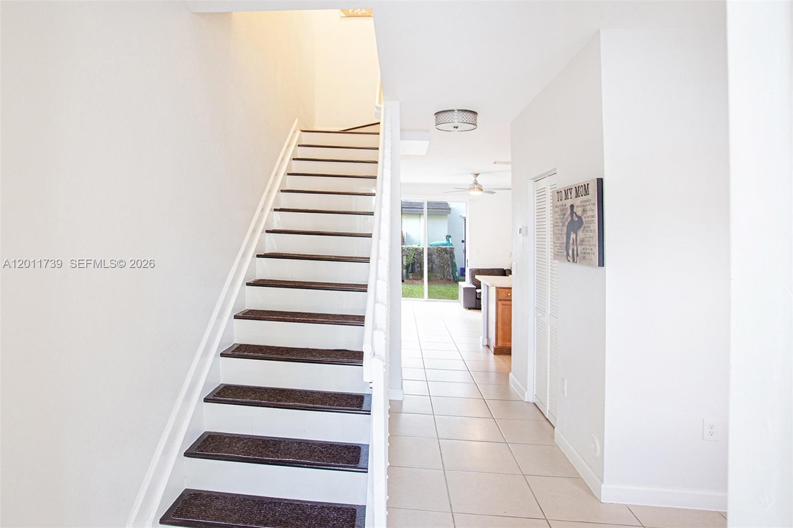 A staircase with brown treads leads upward beside a hallway with white tiled floors — 132 SE 28th Pl # 7, Homestead FL 33033, HOMESTEAD, FL