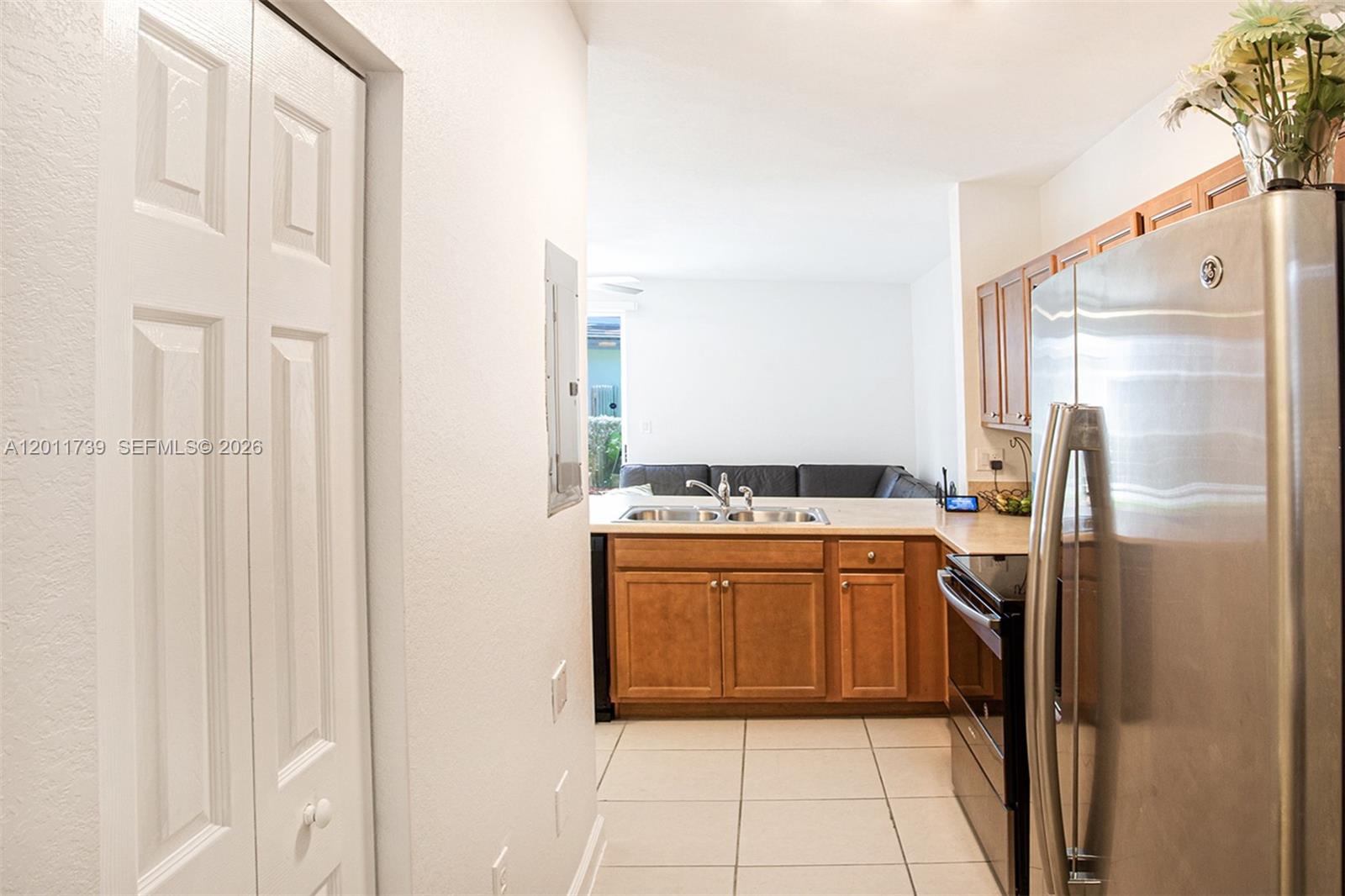 A kitchen with wooden cabinets, stainless steel appliances, and tile flooring overlooks a living area — 132 SE 28th Pl # 7, Homestead FL 33033, HOMESTEAD, FL