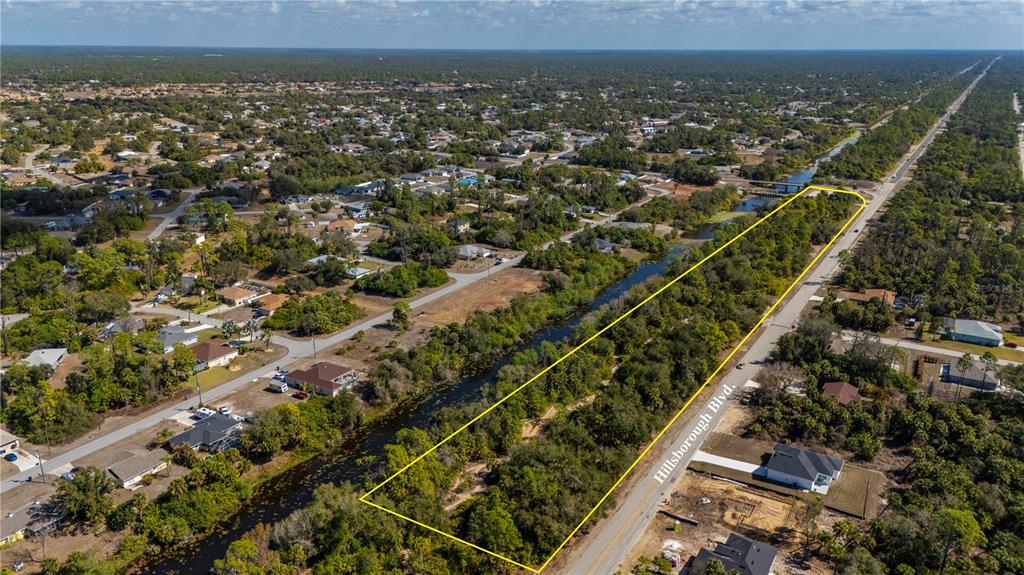 An aerial view shows a rectangular, tree-covered vacant lot bordered by a road and canal — W HILLSBOROUGH BOULEVARD, NORTH PORT, FL