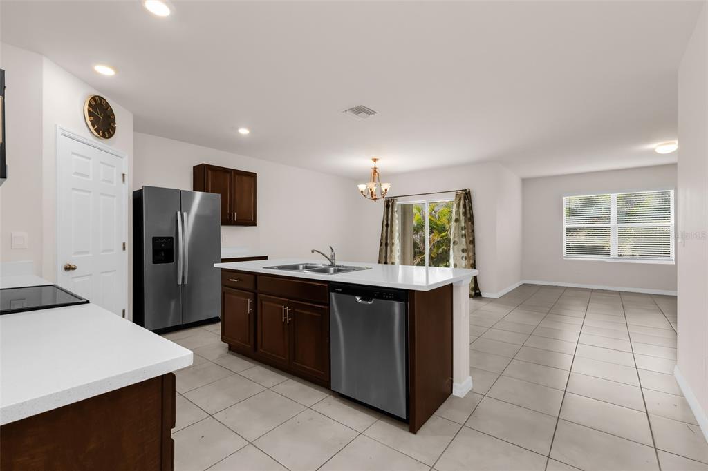 A kitchen with dark wood cabinets, stainless steel appliances, and tile flooring opens to a dining area — 26567 DEEP CREEK BOULEVARD, PUNTA GORDA, FL