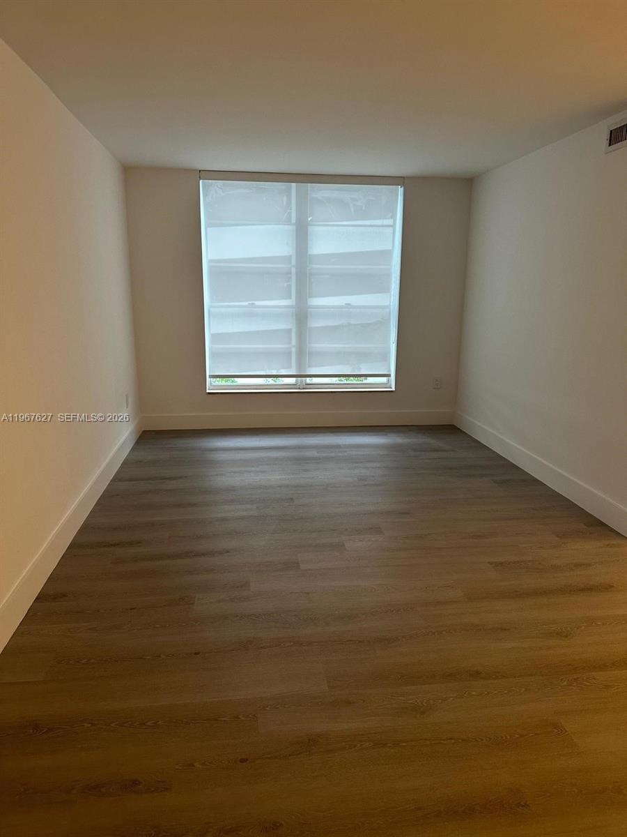 An empty room features light wood-look flooring, white walls, and a large window with blinds — 210 SW 11th St # 510, Miami FL 33130, MIAMI, FL