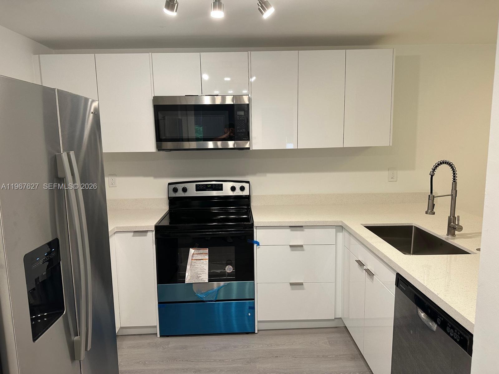 A modern kitchen features white flat-panel cabinets, stainless steel appliances, and light-colored quartz countertops — 210 SW 11th St # 510, Miami FL 33130, MIAMI, FL