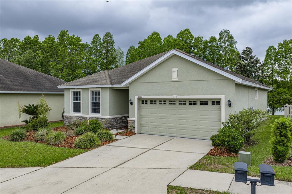 A single-story house with light green stucco siding, a two-car garage, and a concrete driveway — 5544 HURON WAY, LAKELAND, FL